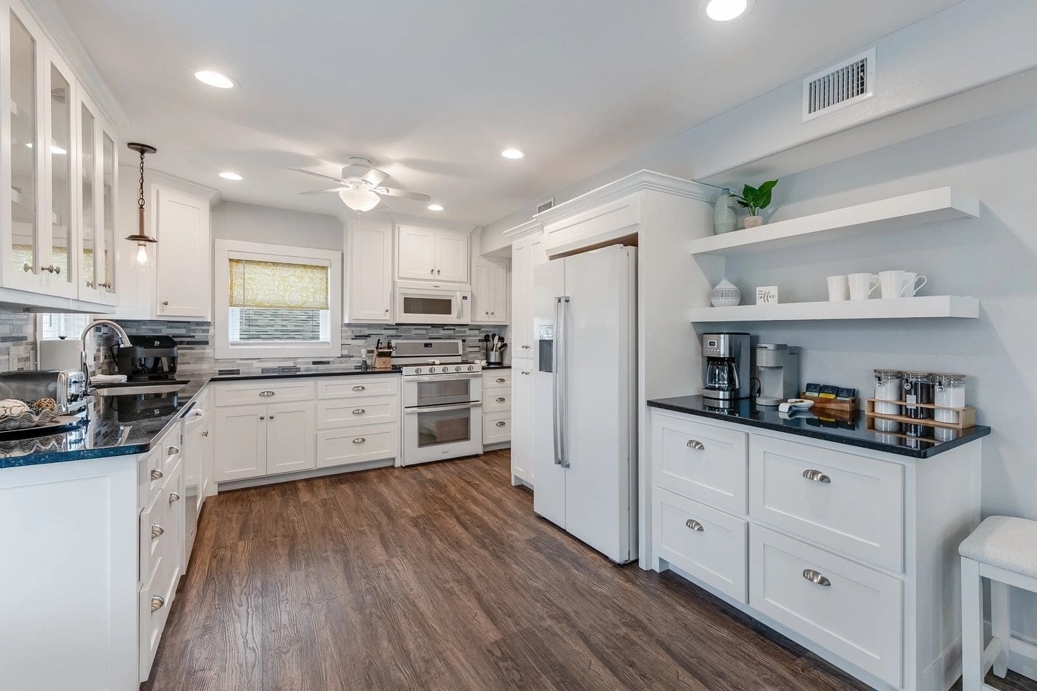 A kitchen with white cabinets and wood floors.